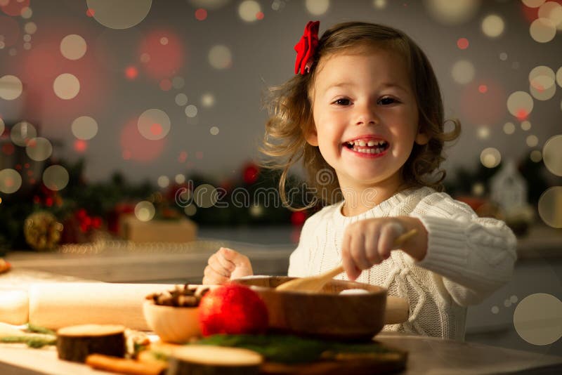 Cute little smiling girl 2-4 with a red bow prepares Christmas gingerbread cookies in the New Year`s kitchen. Cute little smiling girl 2-4 with a red bow prepares Christmas gingerbread cookies in the New Year`s kitchen