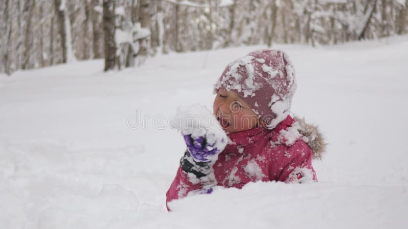 Den lilla flickan sitter i snödrift och äter snö