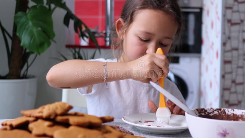 Den lilla flickan tar sirap med kulinarisk borste och applicerar den på gingerbröd