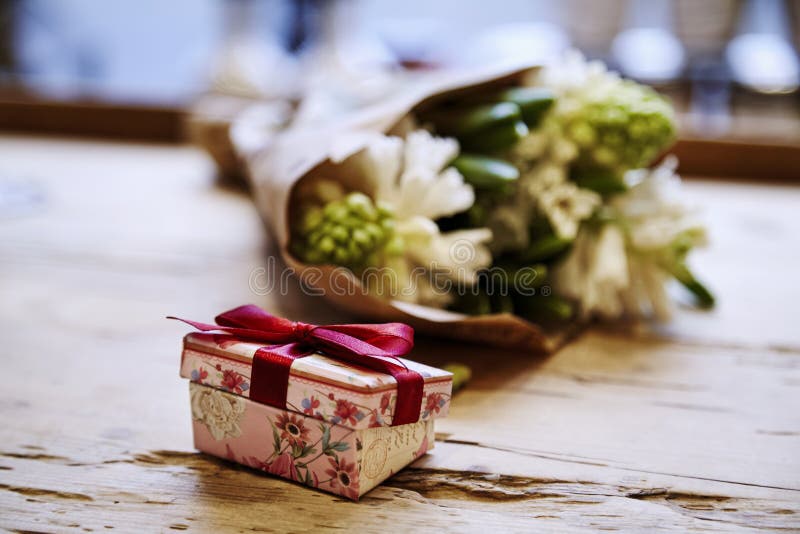 Den lilla gulliga närvarande asken med pilbågen på trätabellen, steg blommor bakom Begrepp för dag för St-valentin` s arkivfoto
