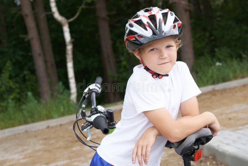 Den lilla kaukasiska pojken i skyddande hjälm som lutar sig mot kamerans cykel Tonåring redo att åka royaltyfria bilder