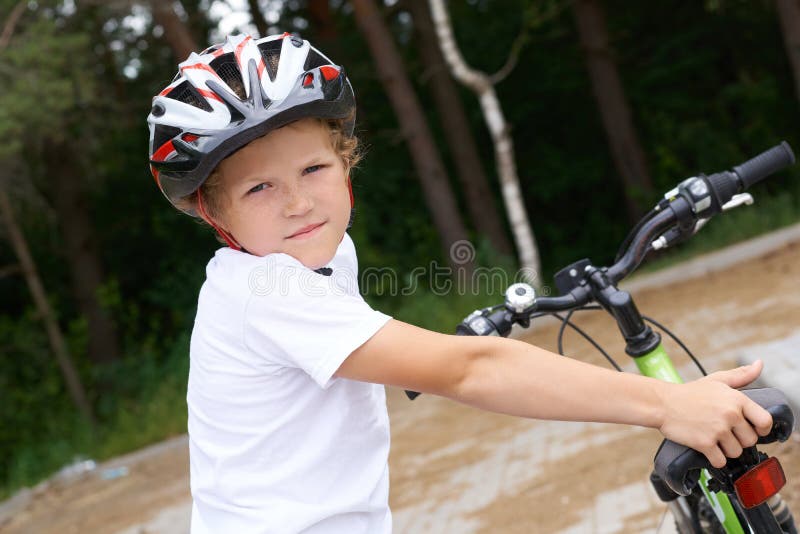 Den lilla kaukasiska pojken i skyddande hjälm som lutar sig mot kamerans cykel Tonåring redo att åka arkivfoton