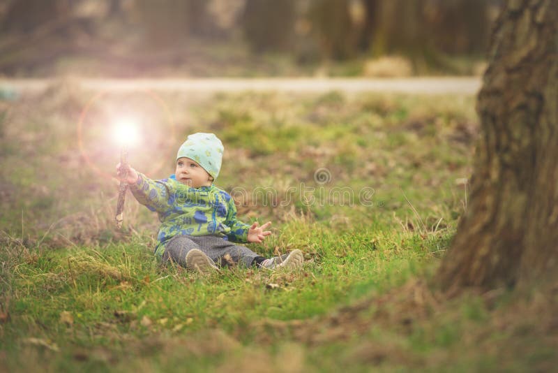 Den lilla pojken sitter på gräs, och behandla trollspöet i vår parkera nära stort träd royaltyfri foto Den lilla pojken sitter på gräs, och behandla trollspöet i vår parkera nära stort träd royaltyfri foto