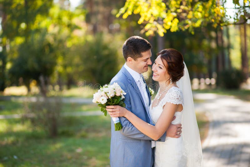 Den lyckliga bruden, brudgumanseende i gräsplan parkerar och att kyssa och att le som skrattar vänner i bröllopdag förbunden lyck