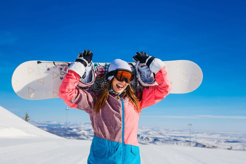Den lyckliga gladlynta kvinnan i skidar dräkten, och exponeringsglas rymmer en snowboard i hennes händer i vinter extremt fotografering för bildbyråer Den lyckliga gladlynta kvinnan i skidar dräkten, och exponeringsglas rymmer en snowboard i hennes händer i vinter extremt fotografering för bildbyråer
