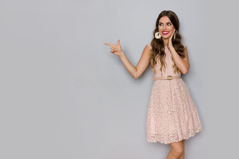 Den lyckliga härliga kvinnan i beiga snör åt Mini Dress Is Looking Away och att peka royaltyfri bild Den lyckliga härliga kvinnan i beiga snör åt Mini Dress Is Looking Away och att peka royaltyfri bild