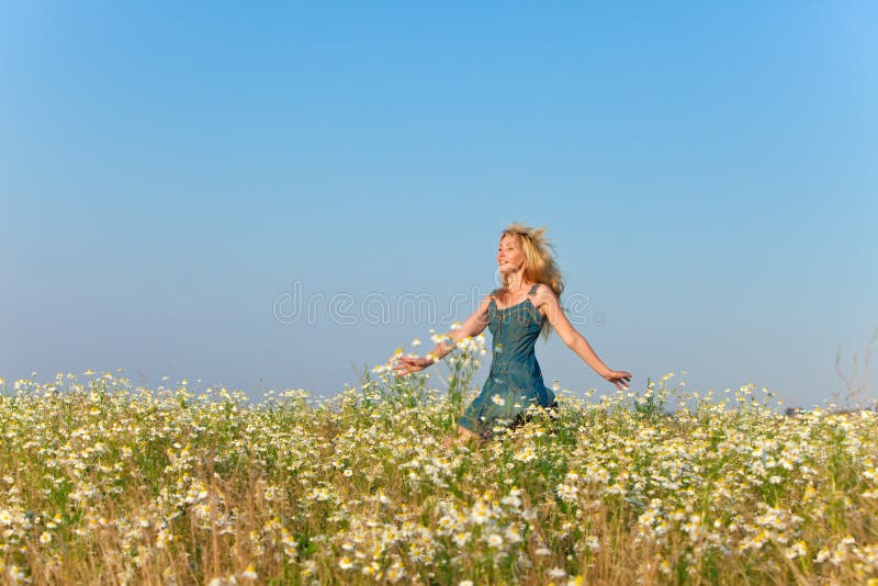 Den lyckliga unga kvinnan i jeans sundress hoppar i fältet av kamomillar i en solig dag fotografering för bildbyråer Den lyckliga unga kvinnan i jeans sundress hoppar i fältet av kamomillar i en solig dag fotografering för bildbyråer