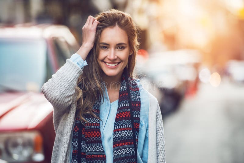 Den lyckliga unga vuxna kvinnan som ler med tänder, ler utomhus och gå på stadsgatan på kläder för vintern för solnedgångtid bära