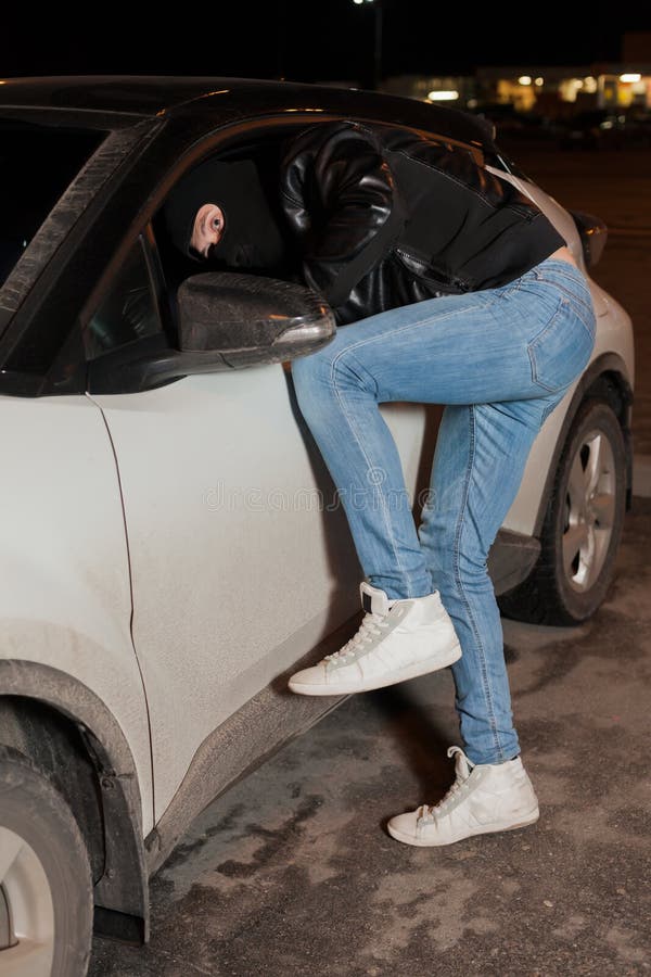 Den manliga tjuven får in i bilen till och med fönstret royaltyfri bild Den manliga tjuven får in i bilen till och med fönstret royaltyfri bild