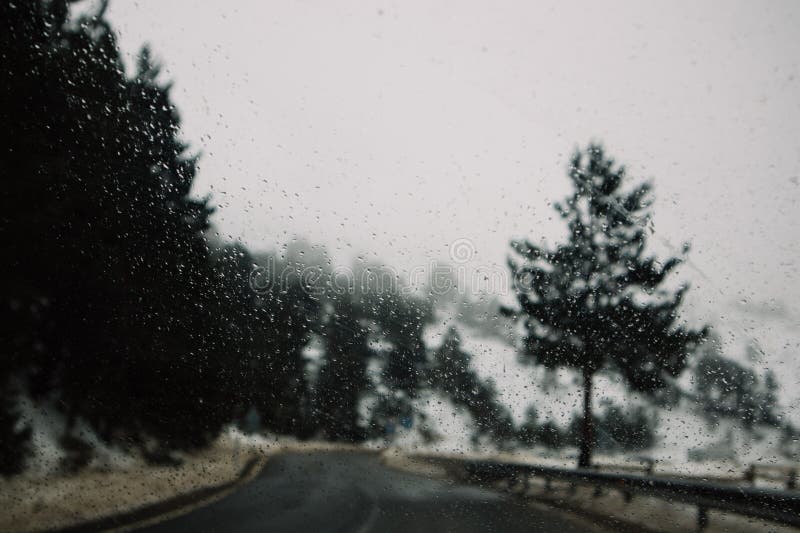 Dark desert asphalt road in a pine forest in a gloomy cold winter day Rain drops on blurry car windshield. Traveling to a ski resort in winter season. Dark desert asphalt road in a pine forest in a gloomy cold winter day Rain drops on blurry car windshield. Traveling to a ski resort in winter season