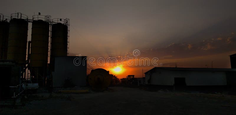 Dark sunset is falling over construction batching plant with black clouds. Silo of batching plant is looking dark in evening. Dark sunset is falling over construction batching plant with black clouds. Silo of batching plant is looking dark in evening