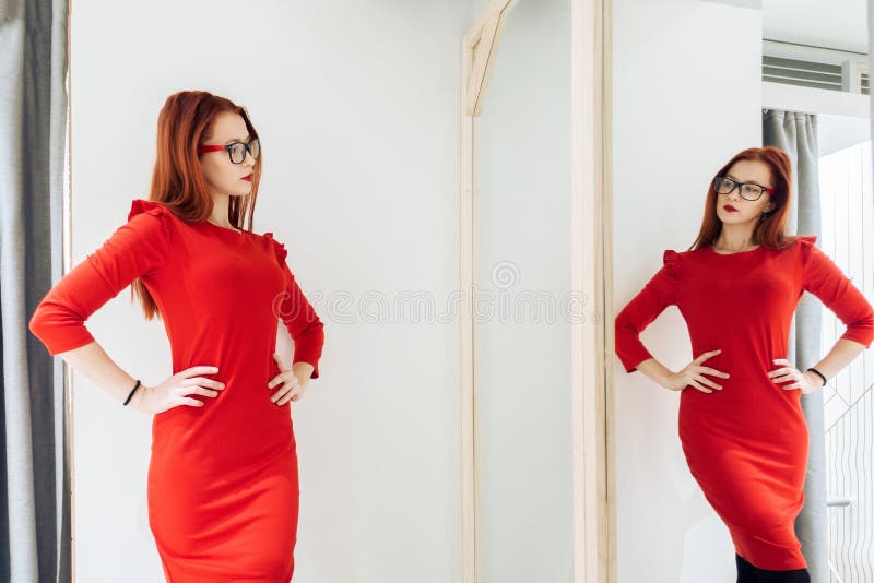 Den nätta kvinnan som försöker på kläder i ett passande, shoppar damen i den röda klänningen reflekteras i spegeln royaltyfri bild Den nätta kvinnan som försöker på kläder i ett passande, shoppar damen i den röda klänningen reflekteras i spegeln royaltyfri bild