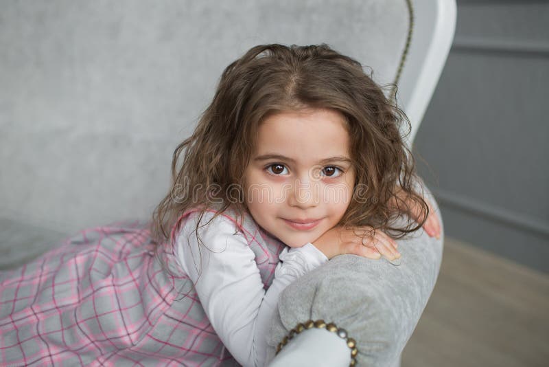 Den nätta lilla flickan med brunt hår sitter på en grå soffa fotografering för bildbyråer Den nätta lilla flickan med brunt hår sitter på en grå soffa fotografering för bildbyråer