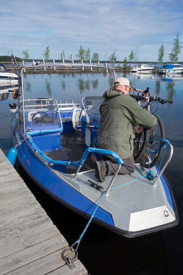 Taipalsaari, Finland – July 2, 2015: Unidentified fishing guide ties touring bikes to a fishing boat in marina by the lake Saimaa, Finland for crossing to the other side of the lake from Taipalsaari. Taipalsaari, Finland – July 2, 2015: Unidentified fishing guide ties touring bikes to a fishing boat in marina by the lake Saimaa, Finland for crossing to the other side of the lake from Taipalsaari.