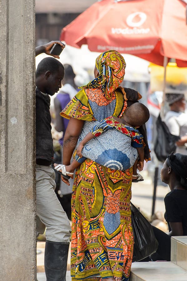 Den oidentifierade ghananska kvinnan bär en behandla som ett barn på den Kumasi marknaden royaltyfria foton