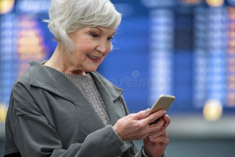 Den positiva höga kvinnlign är den hållande mobiltelefonen med leende royaltyfri foto Den positiva höga kvinnlign är den hållande mobiltelefonen med leende royaltyfri foto