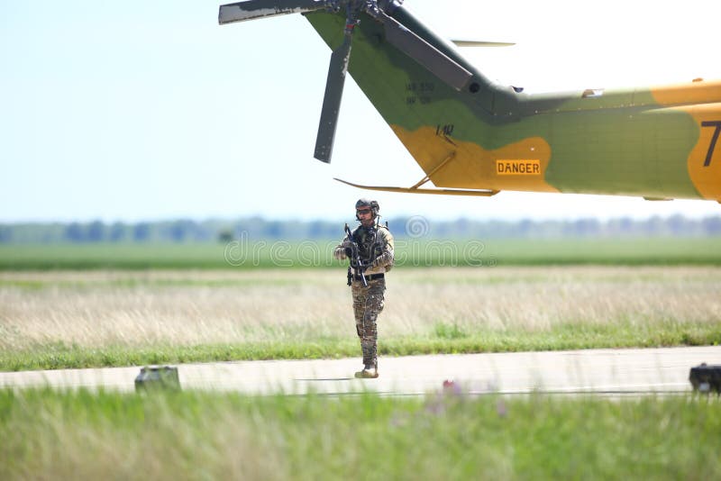 Den rumänska soldaten patrullerar en militärflygbas nära en militär helikopter under en övning royaltyfri fotografi Den rumänska soldaten patrullerar en militärflygbas nära en militär helikopter under en övning royaltyfri fotografi