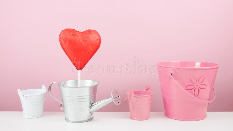 Den röda omkullkastade chokladhjärtapinnen med liten silver som bevattnar kan, och små rosa färger ösregnar arkivfoton Den röda omkullkastade chokladhjärtapinnen med liten silver som bevattnar kan, och små rosa färger ösregnar arkivfoton