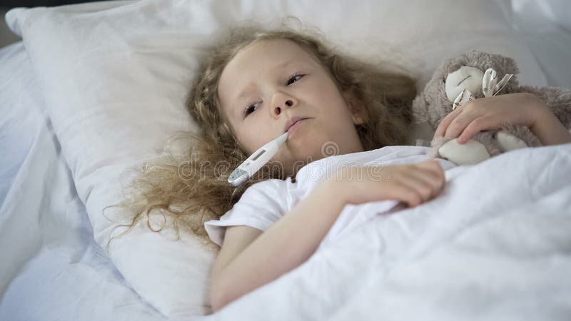 Den sjuka lilla flickan som ligger i säng som var ledsen med termometern i mun, unge fångade kallt royaltyfri bild Den sjuka lilla flickan som ligger i säng som var ledsen med termometern i mun, unge fångade kallt royaltyfri bild