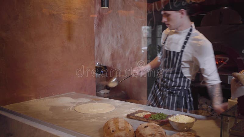 Den skickliga pizzatillverkaren lagar mat deg på modernt restaurangkök bak exponeringsglas Grabben häller mjölkar på formen för