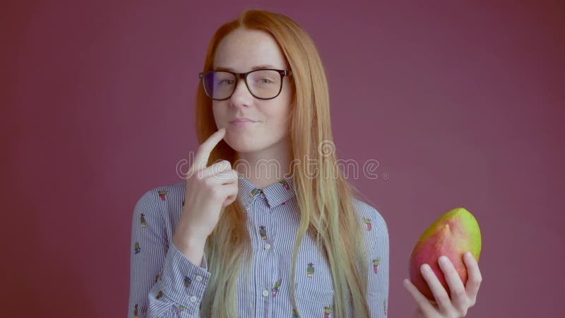 Den smarta ljust rödbrun unga kvinnan i exponeringsglas rekommenderar att äta mango stock video