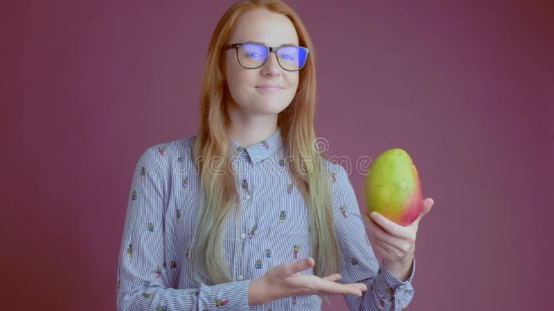 Den smarta ljust rödbrun unga kvinnan i exponeringsglas rekommenderar att äta mango arkivfilmer