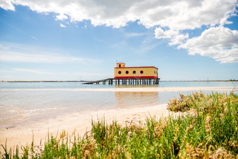 Den soliga strandsikten av den historiska liv-vakten byggnaden i Fuseta, Ria Formosa Natural parkerar, Portugal royaltyfri fotografi Den soliga strandsikten av den historiska liv-vakten byggnaden i Fuseta, Ria Formosa Natural parkerar, Portugal royaltyfri fotografi