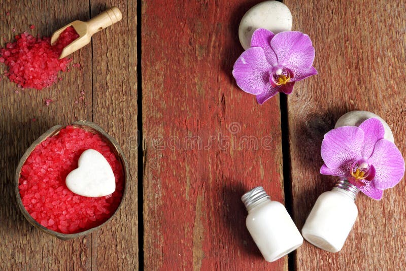 Den Spa uppsättningen på en trätabell med rött salt för bad, lotion för hud och orkidé blommar på stenar, kopieringsutrymme för d arkivbilder Den Spa uppsättningen på en trätabell med rött salt för bad, lotion för hud och orkidé blommar på stenar, kopieringsutrymme för d arkivbilder