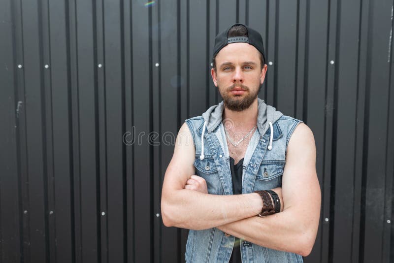 Den stiliga unga hipsteren som mannen i en trendig blå grov bomullstvill tilldelar enskjorta med ett skägg i ett svart stilfullt arkivbilder Den stiliga unga hipsteren som mannen i en trendig blå grov bomullstvill tilldelar enskjorta med ett skägg i ett svart stilfullt arkivbilder