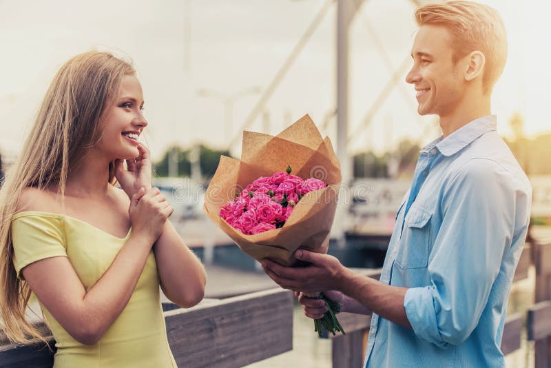 Den stiliga unga mannen ger blommor till den härliga flickan arkivbild Den stiliga unga mannen ger blommor till den härliga flickan arkivbild