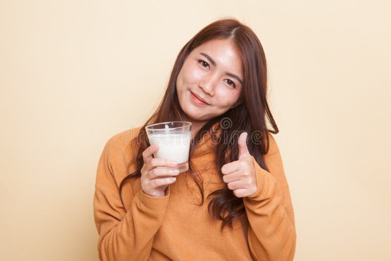 Den sunda asiatiska kvinnan som dricker ett exponeringsglas av, mjölkar upp tummar