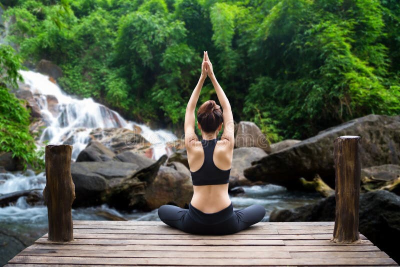 Den sunda kvinnalivsstilen balanserade övning mediterar och zenenergiyoga på bron i morgon vattenfallet i naturskog