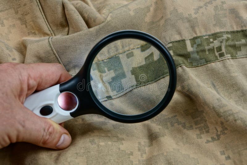 den svarta förstoringsapparaten i handen ökar det bruna gröna rynkiga tyget på kläderna med en söm royaltyfria foton den svarta förstoringsapparaten i handen ökar det bruna gröna rynkiga tyget på kläderna med en söm royaltyfria foton