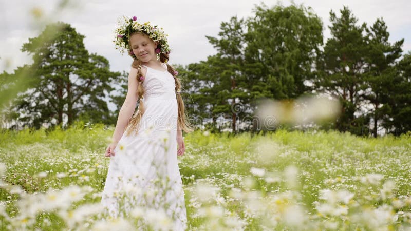 Den tonåriga flickan med tusenskönakransen på hennes huvud går på äng med blommor