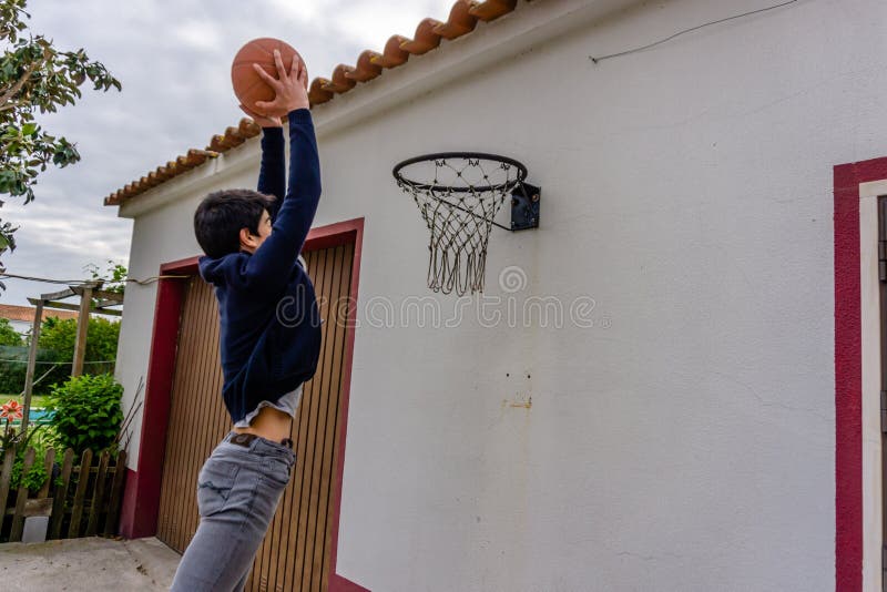 Den tonårs- pojken skjuter basketen in mot beslaget som monteras ovanför garagedörren arkivfoto Den tonårs- pojken skjuter basketen in mot beslaget som monteras ovanför garagedörren arkivfoto