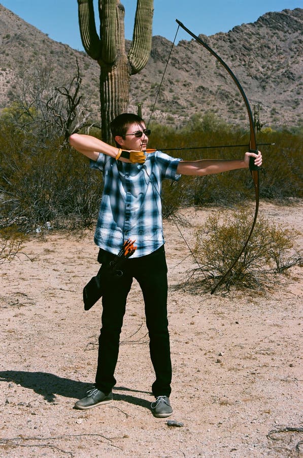 Young man shooting a long bow style bow and arrow in the desert. Young man shooting a long bow style bow and arrow in the desert