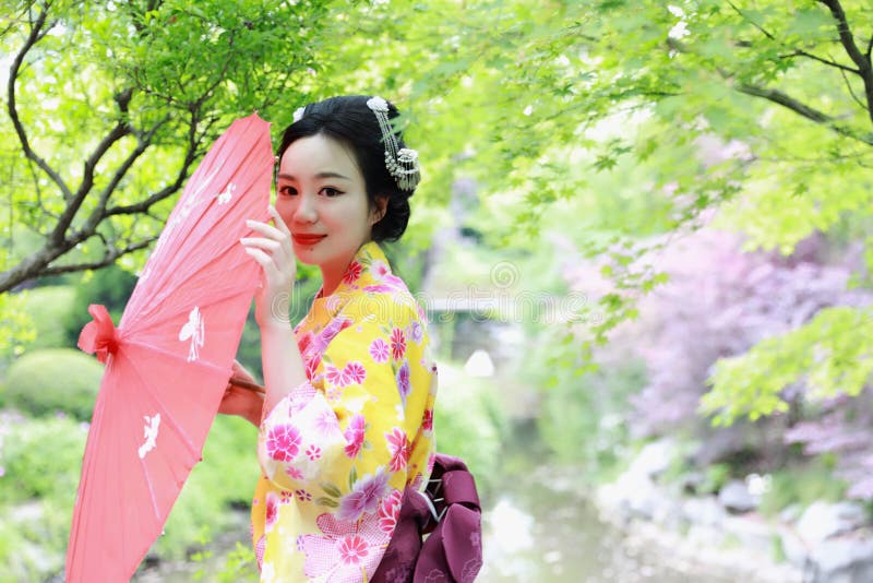 Den traditionella asiatiska japanska härliga Geishakvinnan bär kimonobruden med ett rött paraply i en graden royaltyfri foto Den traditionella asiatiska japanska härliga Geishakvinnan bär kimonobruden med ett rött paraply i en graden royaltyfri foto