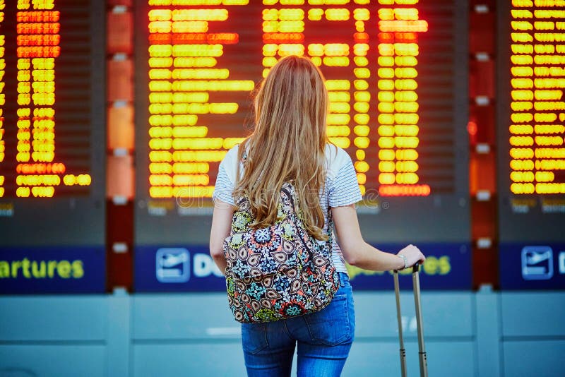 Den turist- flickan med ryggsäcken och bär på bagage i internationell flygplats, nära informationsbräde om flyg royaltyfri fotografi Den turist- flickan med ryggsäcken och bär på bagage i internationell flygplats, nära informationsbräde om flyg royaltyfri fotografi