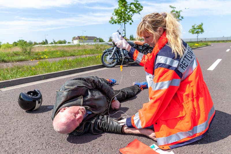 Den tyska personen med paramedicinsk utbildning hjälper en sårad motorcyklist arkivbild Den tyska personen med paramedicinsk utbildning hjälper en sårad motorcyklist arkivbild