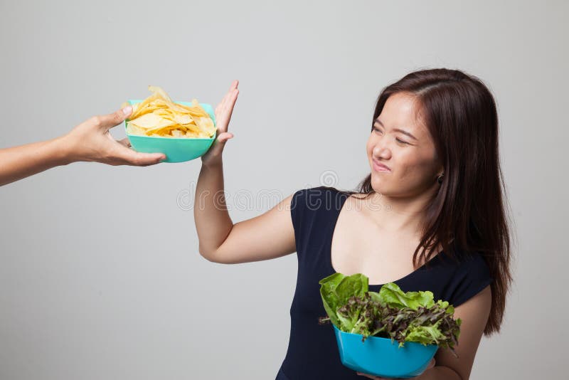 Den unga asiatiska kvinnan med sallad säger inte till potatischiper