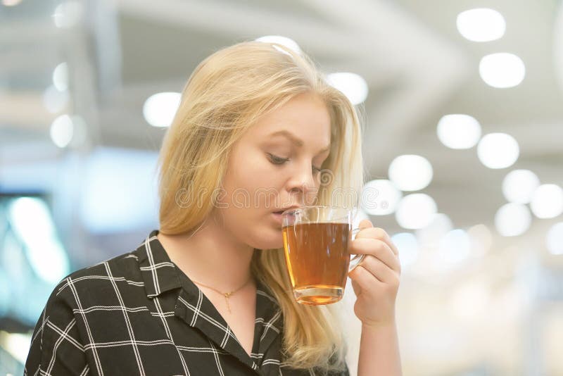 Den unga blonda flickan dricker te i ett kafé royaltyfri fotografi Den unga blonda flickan dricker te i ett kafé royaltyfri fotografi