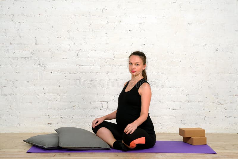 Den unga gravida kvinnan sitter i lotusblommaposition på matt yoga royaltyfria bilder Den unga gravida kvinnan sitter i lotusblommaposition på matt yoga royaltyfria bilder