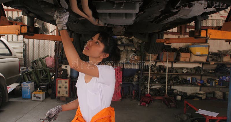 Den unga härliga bilmekanikern kontrollerar bilchassivägen i garage