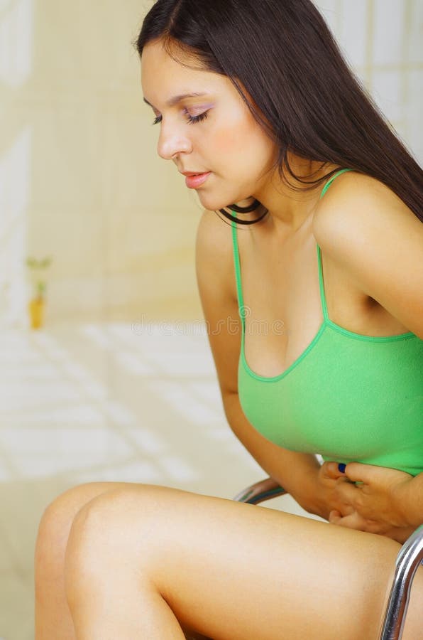 Den unga härliga latinamerikanska kvinnan i det smärtsamma uttryckt som trycker på hennes buk som lider menstruations- period, sm