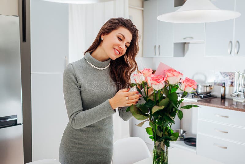Den unga kvinnan grundar buketten av rosor med kortet på kök Lycklig flickaläsninganmärkning i blommor red steg arkivfoton
