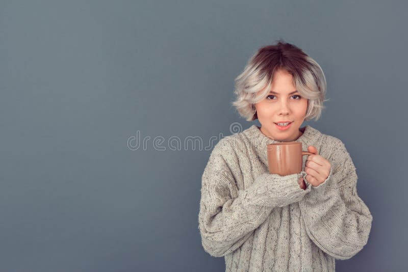 Den unga kvinnan i en woolen tröja som isoleras på gråa det varma väggvinterbegreppet, mjölkar fotografering för bildbyråer Den unga kvinnan i en woolen tröja som isoleras på gråa det varma väggvinterbegreppet, mjölkar fotografering för bildbyråer