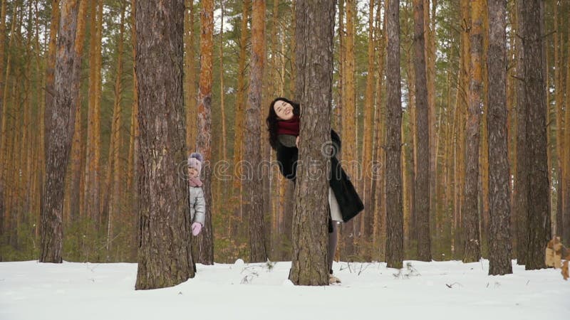 Den unga kvinnan med hennes dotter plirar ut ur trädet i vinterskog