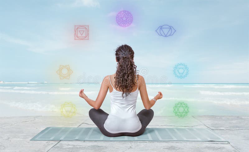 Den unga kvinnan mediterar på stranden med chakras som glöder runt om henne royaltyfria foton Den unga kvinnan mediterar på stranden med chakras som glöder runt om henne royaltyfria foton