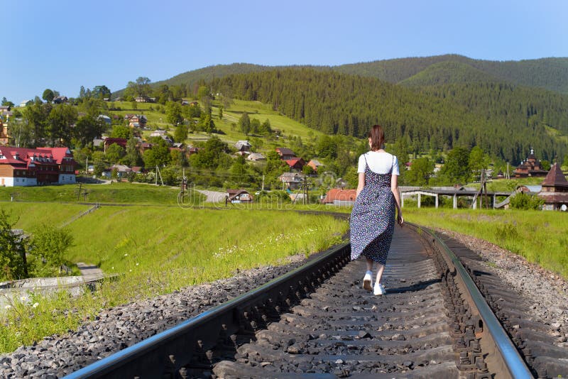 Den unga kvinnan promenerar järnvägsspåren gröna berg arkivfoto Den unga kvinnan promenerar järnvägsspåren gröna berg arkivfoto