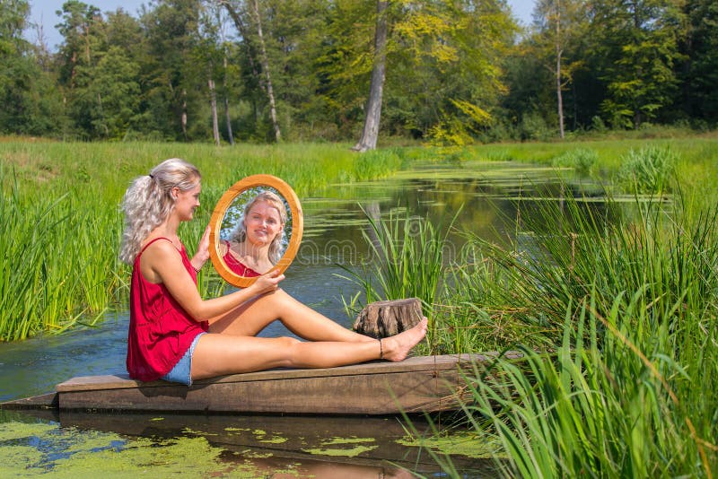 Den unga kvinnan sitter med spegeln på vatten i natur arkivbilder Den unga kvinnan sitter med spegeln på vatten i natur arkivbilder